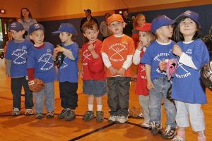 Young children in gym wearing baseball uniforms and gloves.