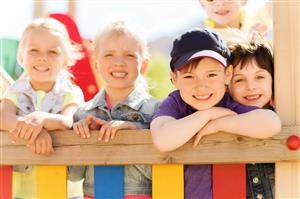Smiling children gathered by a  playground fence